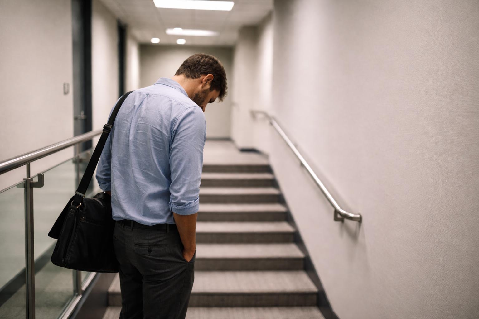 Person standing alone on an office stairwell looking tired