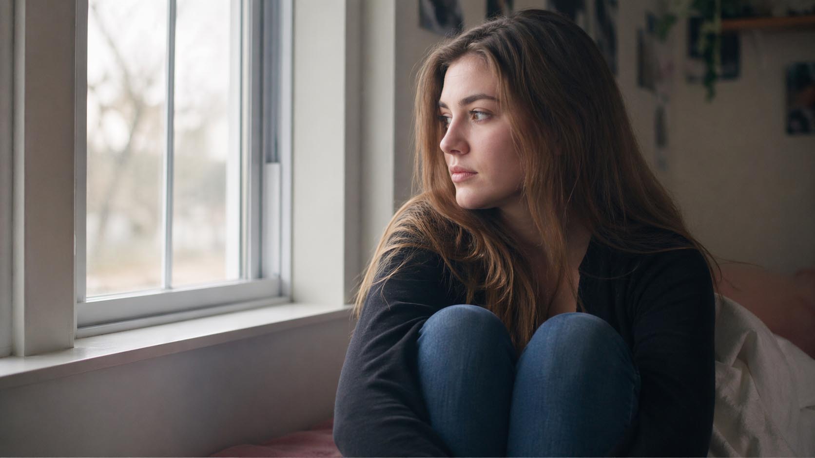 Mlada osoba zamišljeno sedi i razmišlja o svojim osećanjima u tišini.