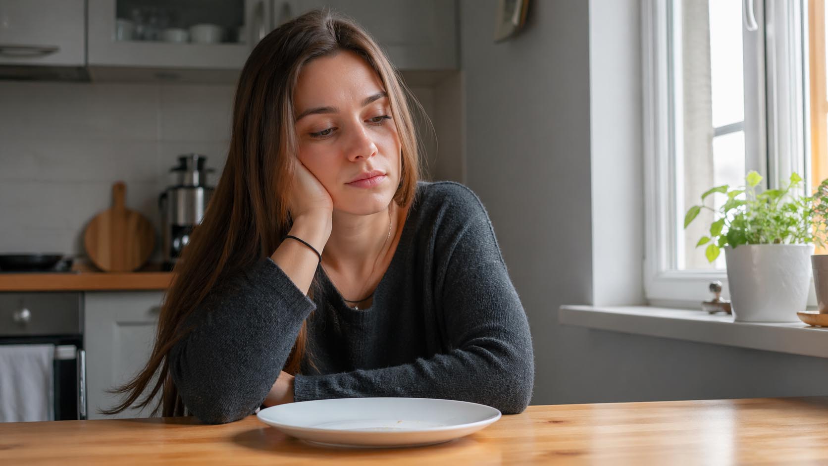 Mlada osoba sedi umorno za stolom sa praznim tanjirom ispred sebe.